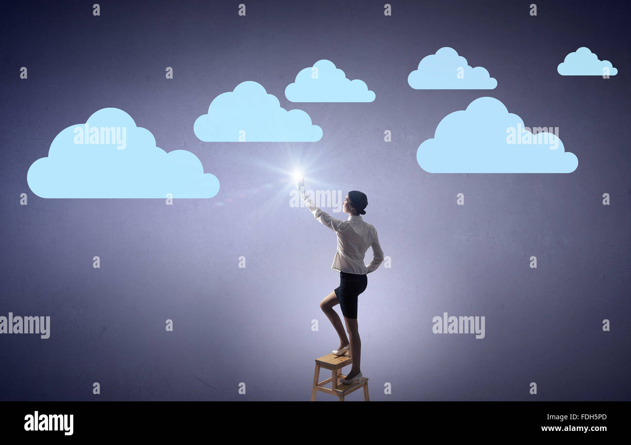 Businesswoman standing on chair and reaching cloud in sky Stock Photo ...