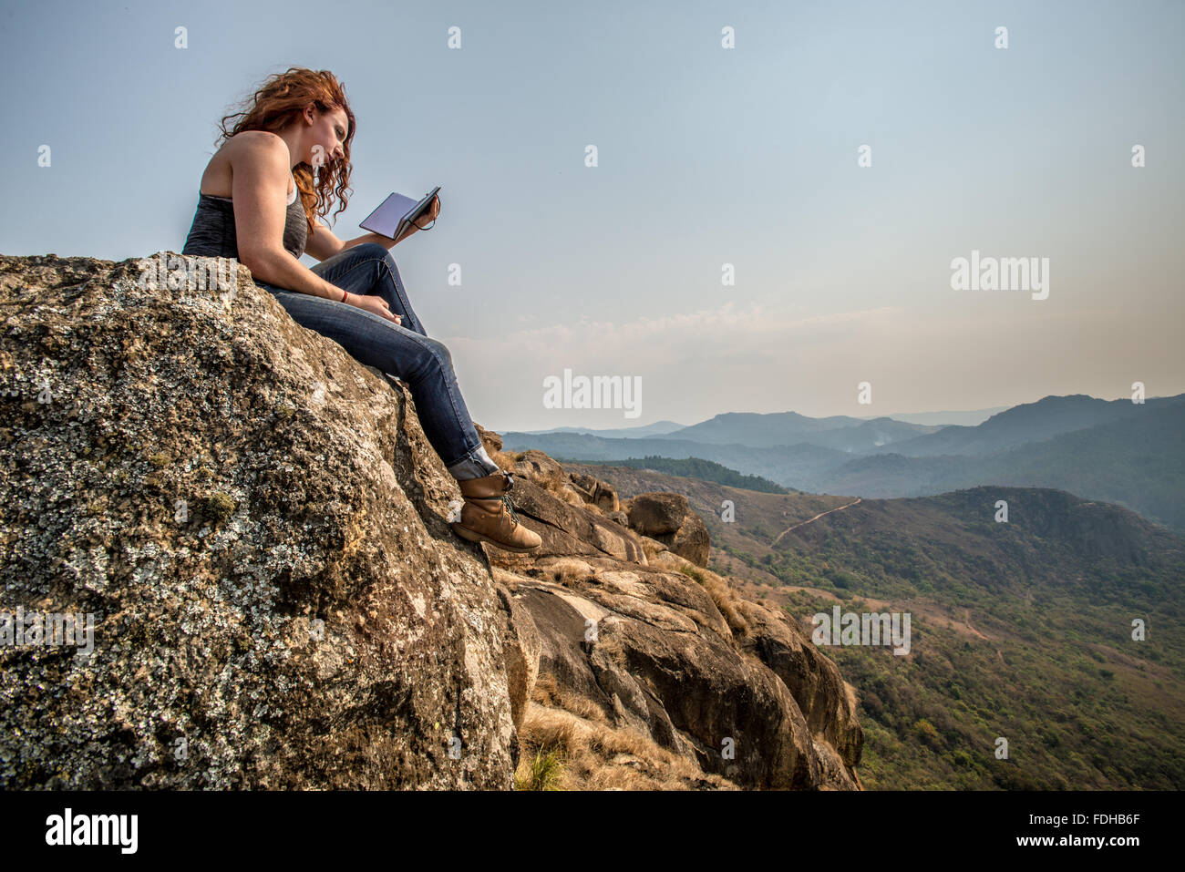 Red-headed girl writing in a journal on top of a boulder at Mlilwane Wildlife Sanctuary in Swaziland, Africa. Stock Photo