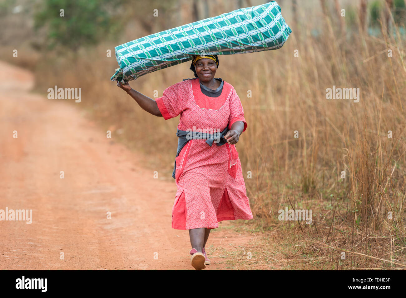 African woman carrying a bag on her head on a dirt road in the Hhohho region of Swaziland, Africa. Stock Photo