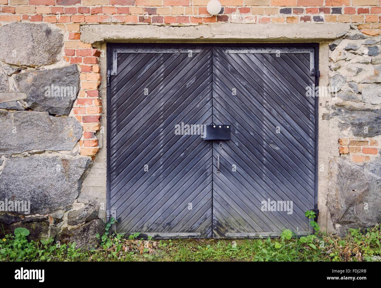 Rustic barn doors and old countryside building exterior. Stone wall constructed with concrete and bricks. Stock Photo