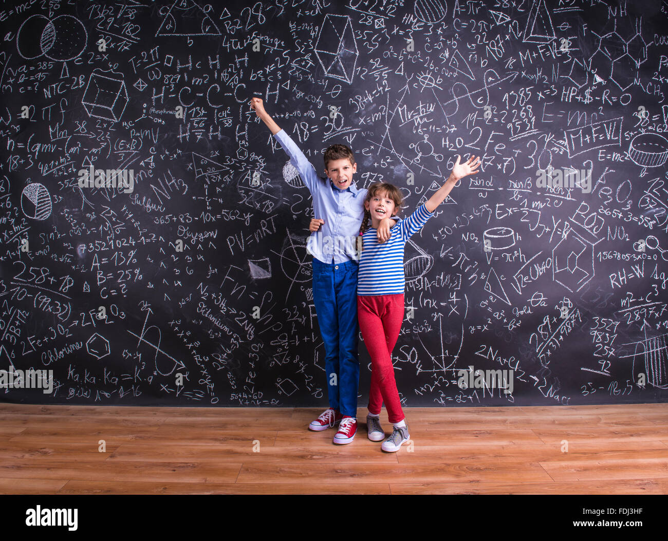 Cute little boy and girl in front of a big blackboard. Stock Photo