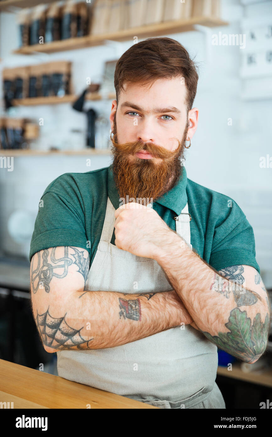 Attractive male barista with tattooed hands standing in coffee shop