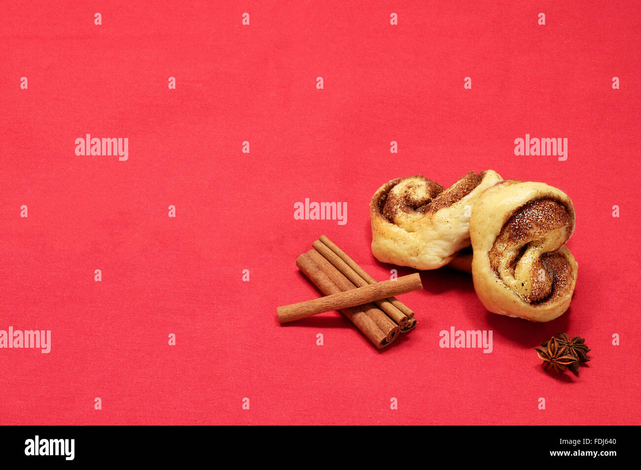 Baked buns with cinnamon and sugar with cinnamon sticks on the red cloth Stock Photo
