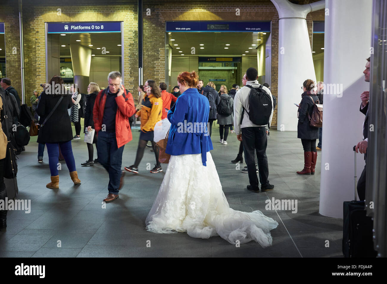 Runaway Bride in blue coat and bridal gown waiting for train at Kings Cross station London, UK. Stock Photo