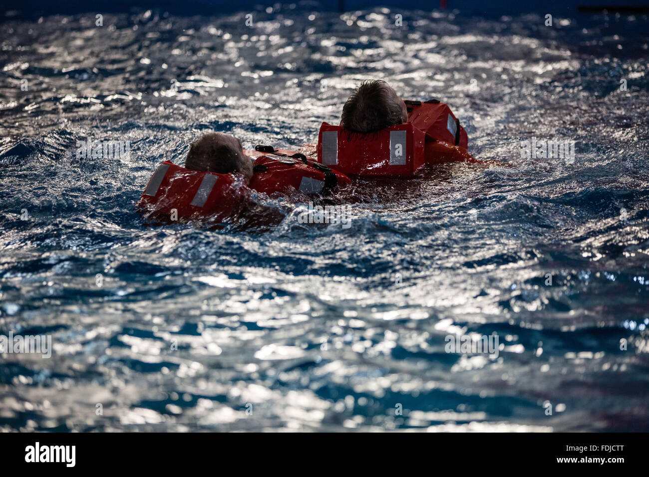 Seafarers and offshore workers wearing life jackets float in a pool during sea survival training
