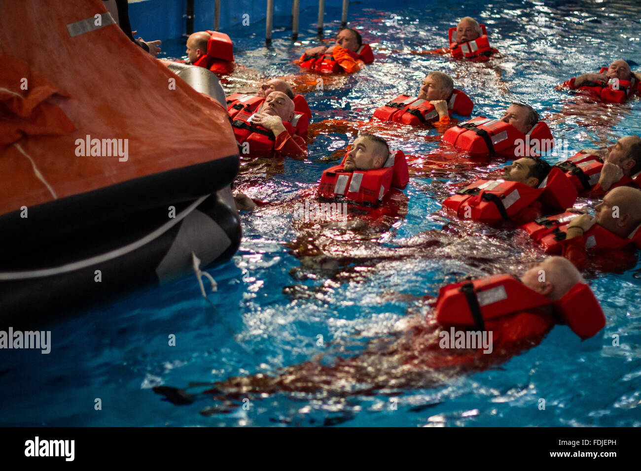 Seafarers and offshore workers wearing life jackets float next to a