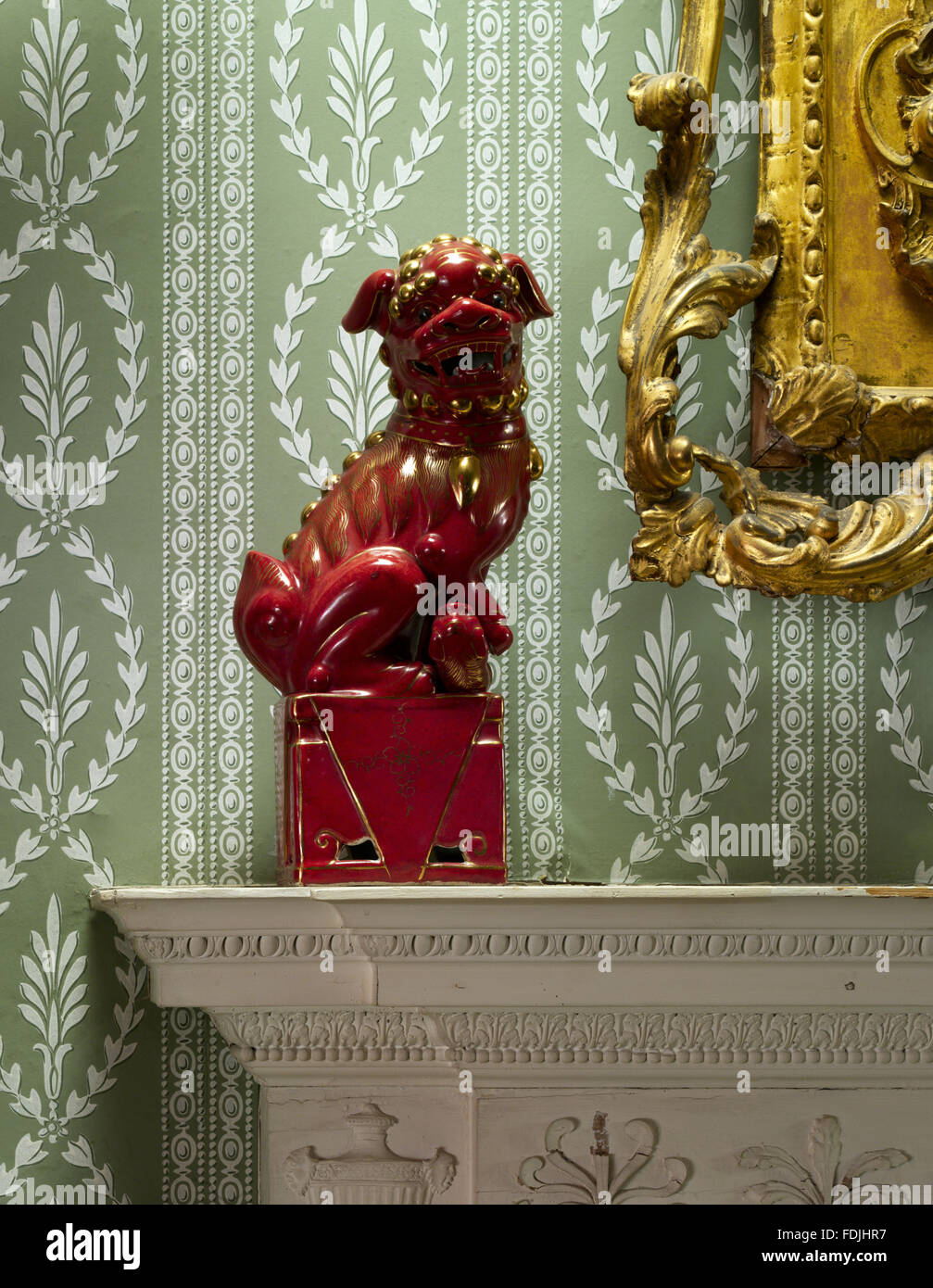Red eighteenth century Chinese ceramic lion on the mantelpiece in the Crimson Bedroom, with 1950s Coles wallpaper behind at Basildon Park, Berkshire. Stock Photo