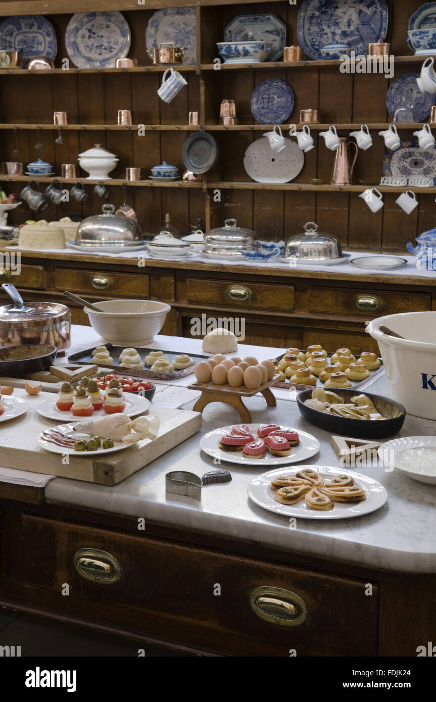 Table in the Kitchen laden with utensils and pastries with the dresser behind at Lanhydrock, Cornwall. Stock Photo
