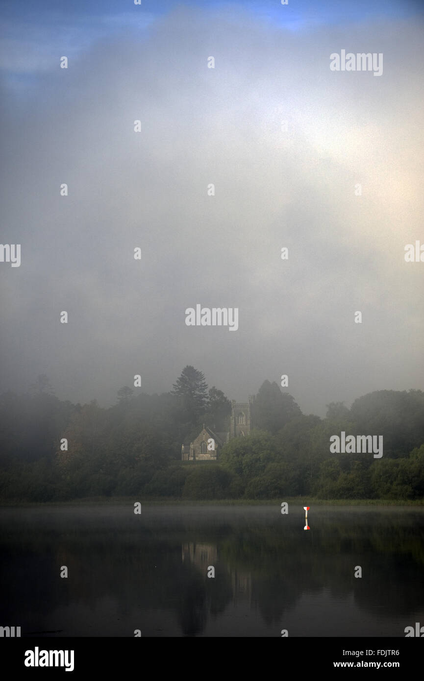 A misty view of Holy Trinity church (not National Trust) on the Derryvore peninsula across Lough Erne at Crom, Co. Fermanagh, Northern Ireland. Stock Photo