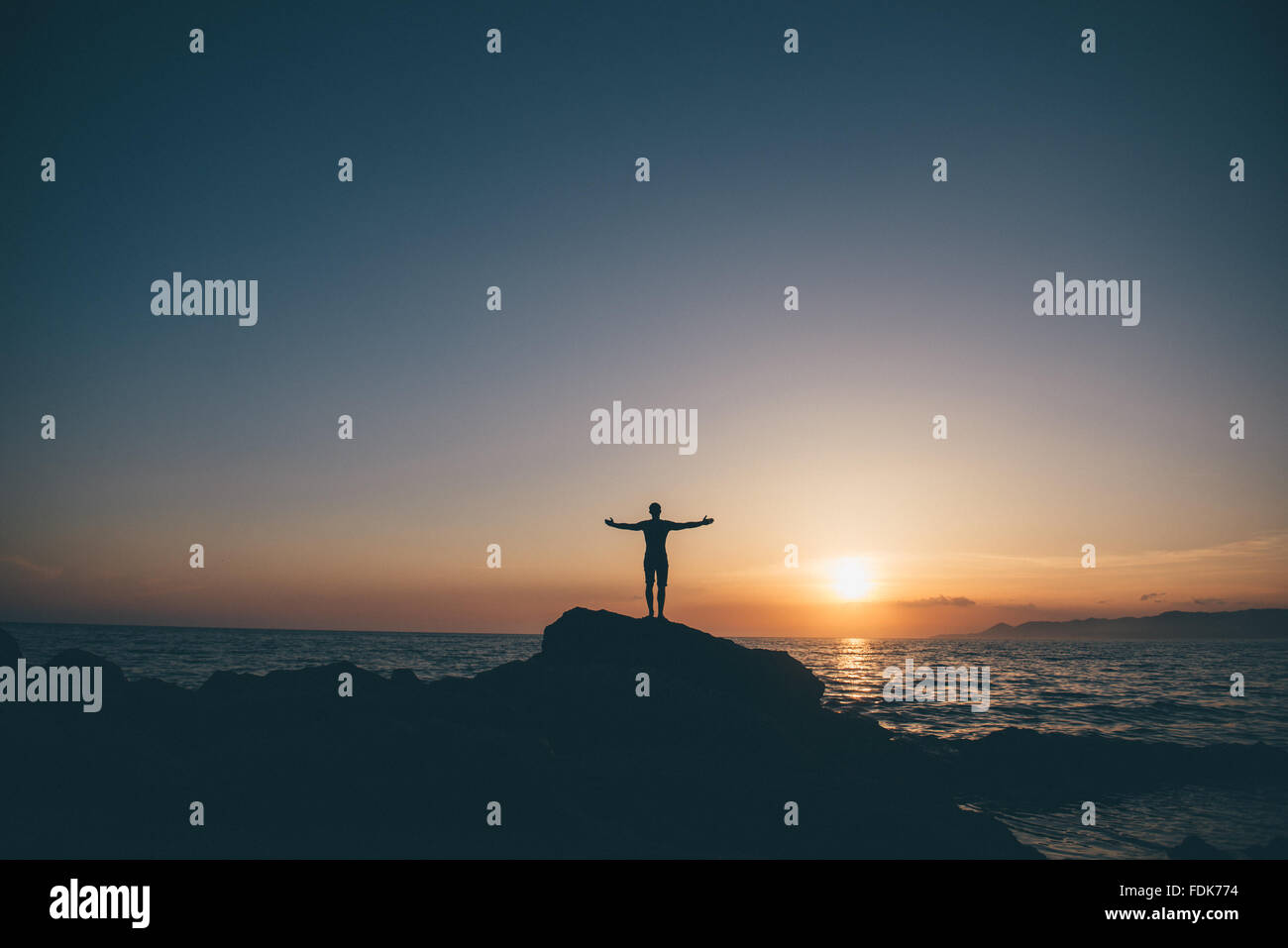 Silhouette of a man standing on rocks with arms outstretched Stock Photo