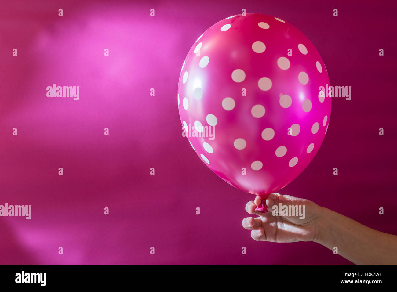 Hand holding pink balloon with white polka dots Stock Photo