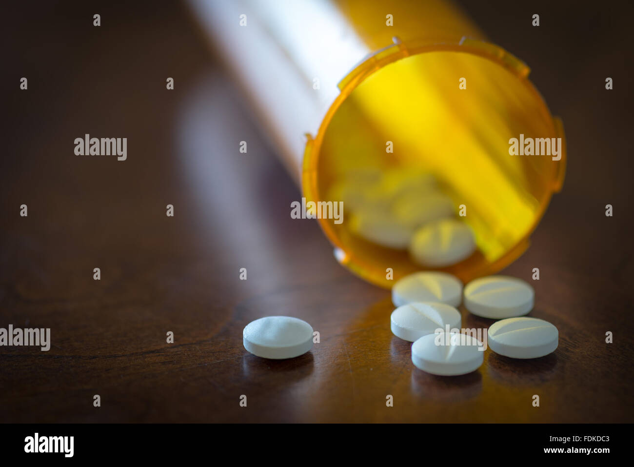 white pills being knocked out of their orange container on top the brown table surface Stock Photo