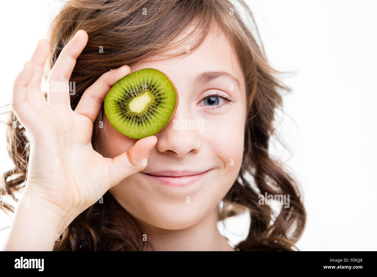 smiling little girl with a kiwi fruit slice over her eye as a joke