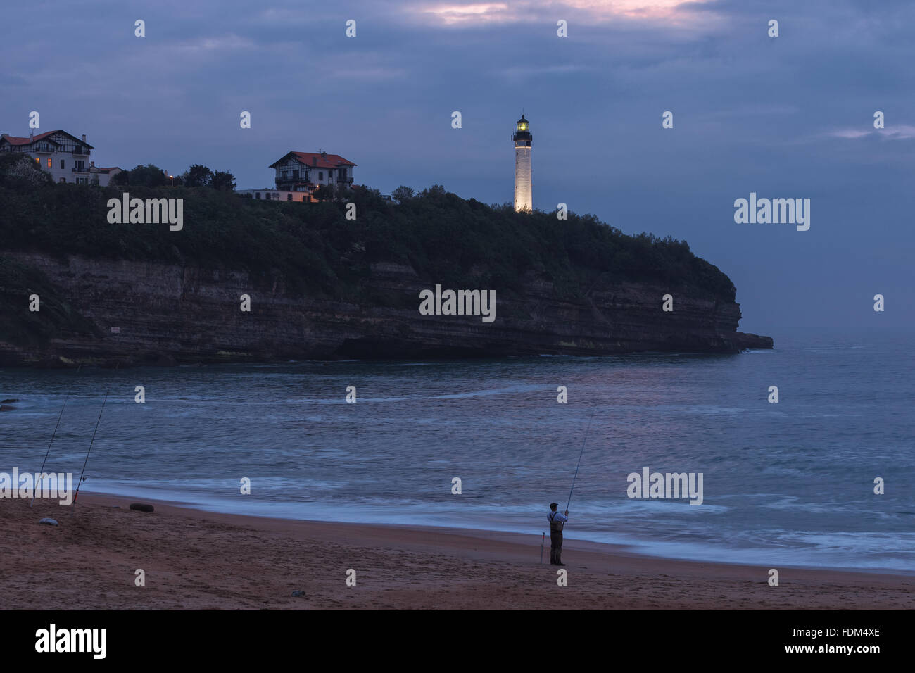 A fisherman in Chambre d'Amour Beach by twilight, with Biarritz Lighthouse in the background. Anglet, Aquitaine, France. Stock Photo