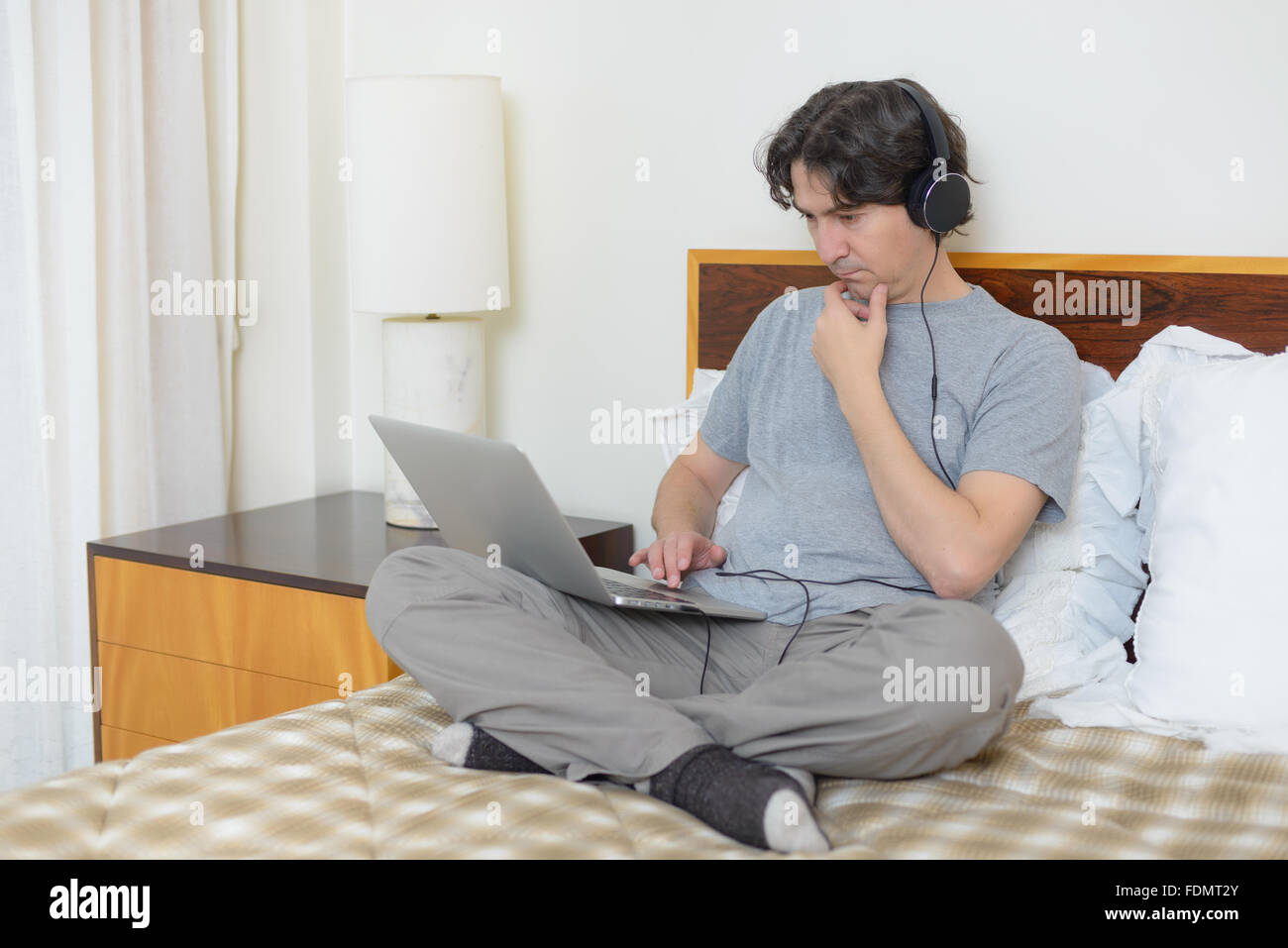 Man sitting in bed working on laptop computer listening to music with headphones Stock Photo Alamy