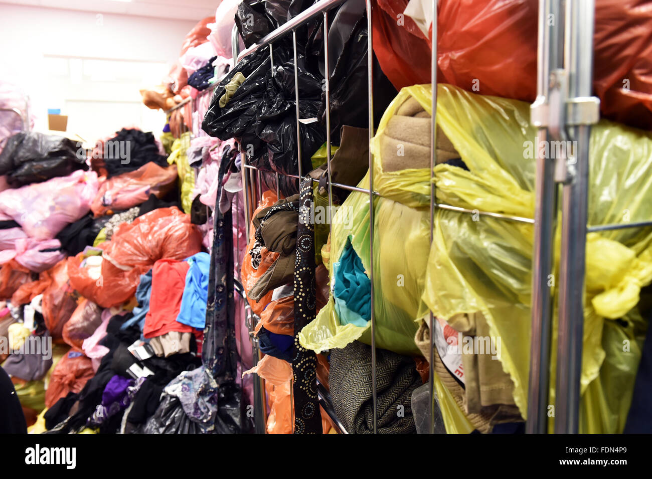 Piles of second hand clothes in plastic bags stacked up at the back of a charity shop UK Stock Photo