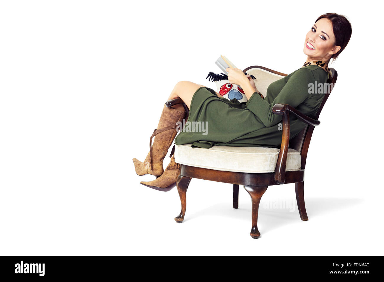 Young woman sitting on chair, holding a book and looking at you. Stock Photo