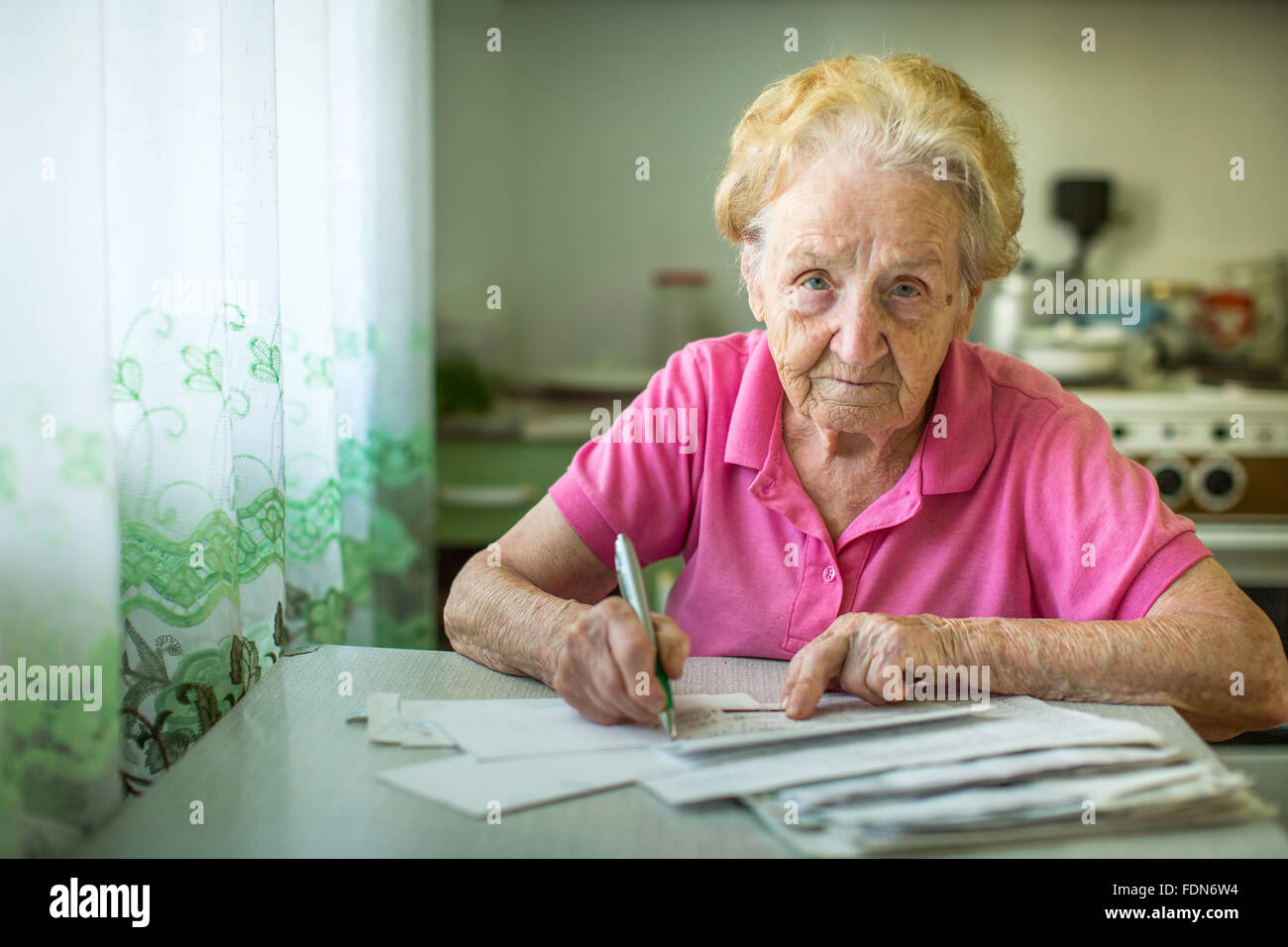 An elderly woman fills in utility bills. Stock Photo