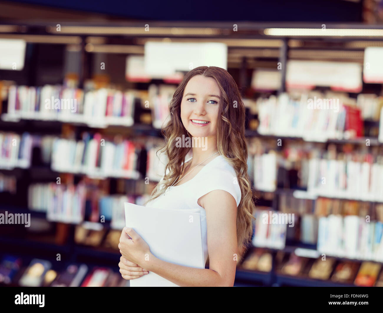 Happy young female student holding books at the library Stock Photo - Alamy