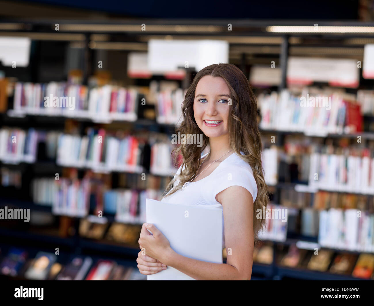 Happy young female student holding books at the library Stock Photo - Alamy