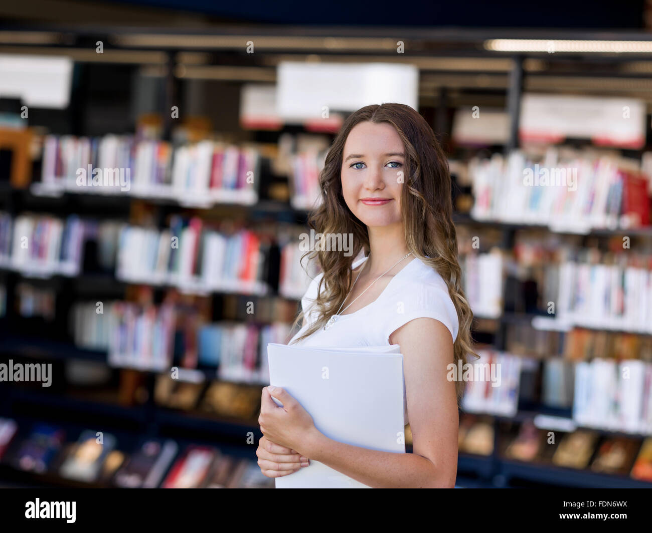 Happy young female student holding books at the library Stock Photo - Alamy