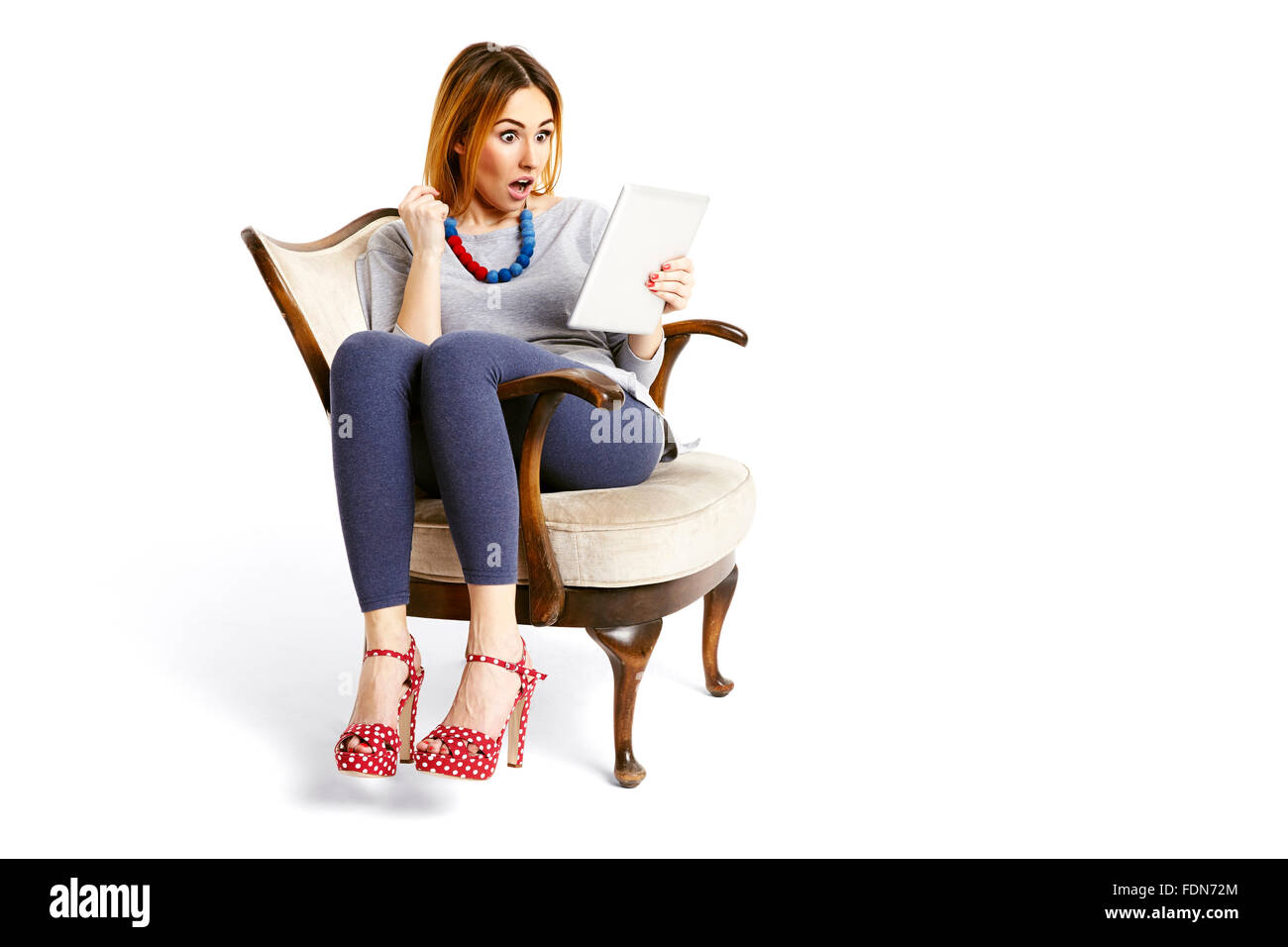 Young woman sitting on a chair watching tablet very surprised and ...