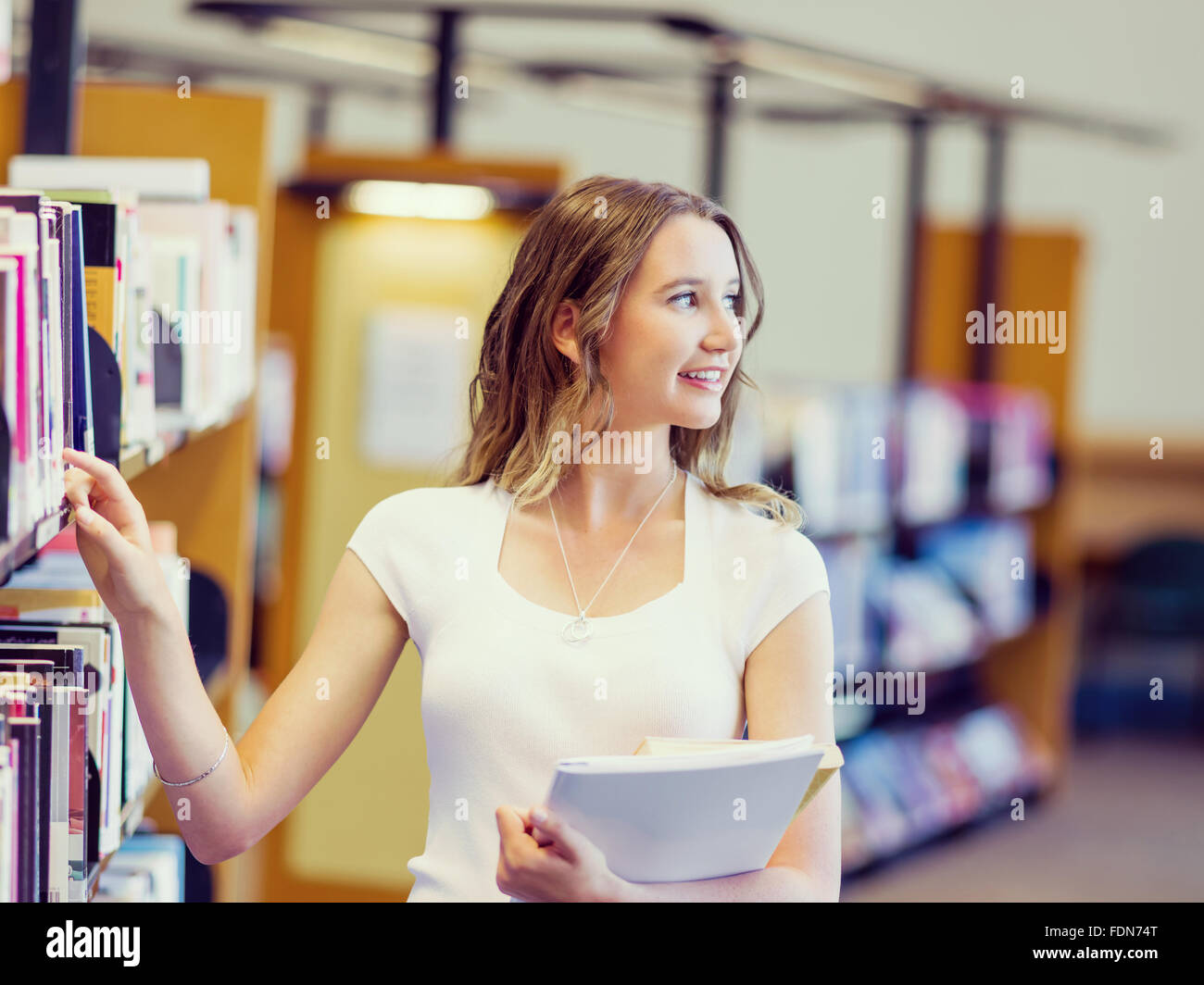 Happy young female student holding books at the library Stock Photo - Alamy