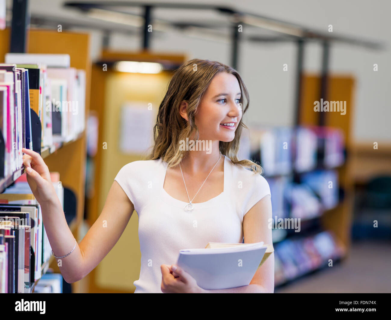 Happy young female student holding books at the library Stock Photo - Alamy