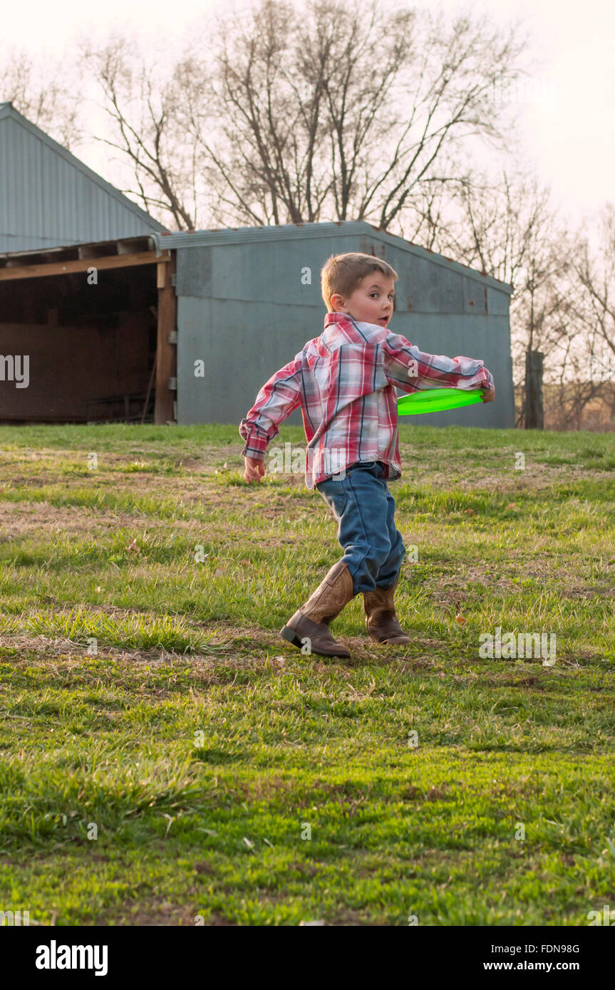 Boy wearing boots throwing frisbee on farm Stock Photo