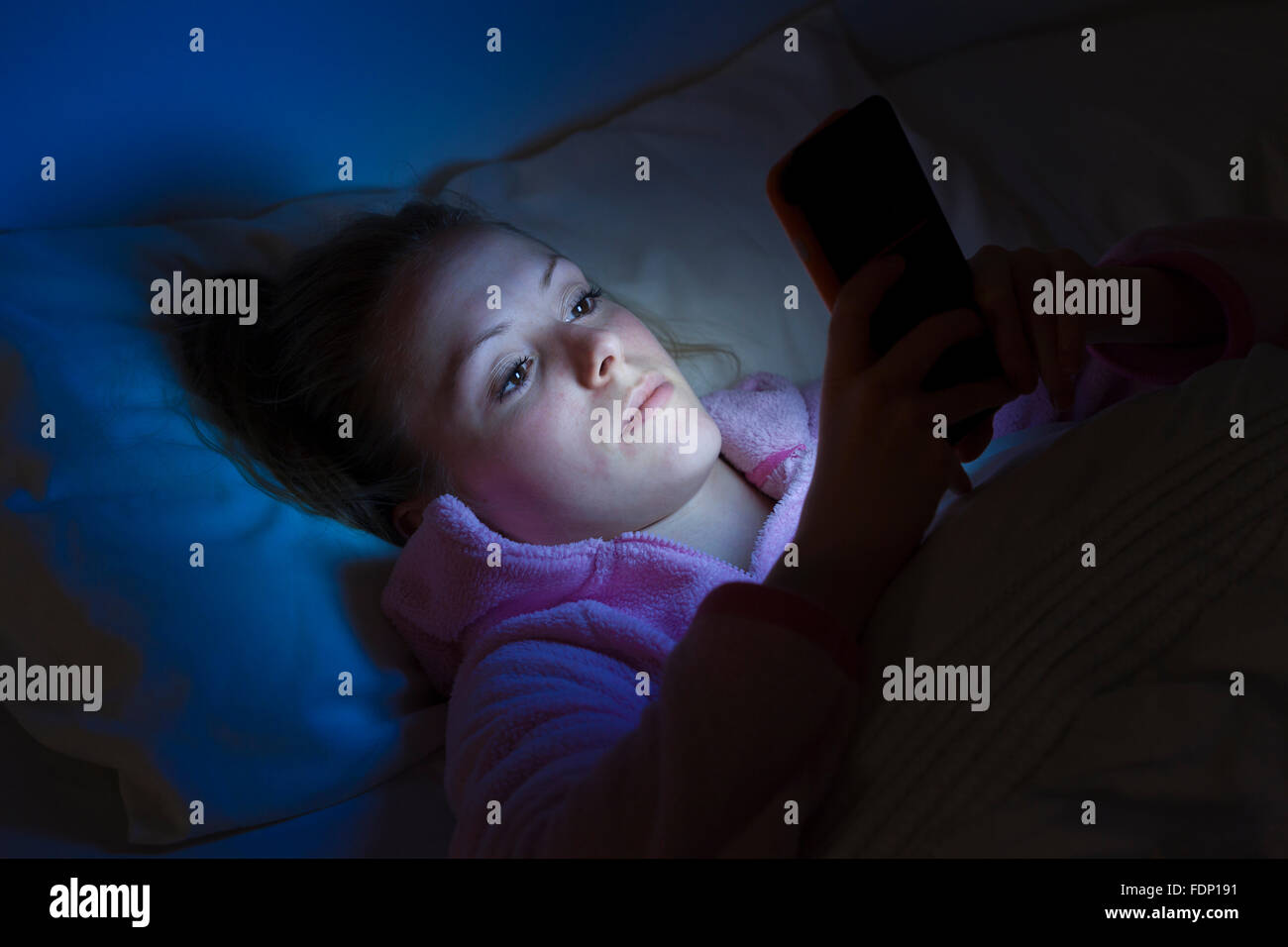 Young teenage girl using smartphone at night in bed. She might be texting watching a movie or surfing the internet.. Use of smartphone at night Stock Photo
