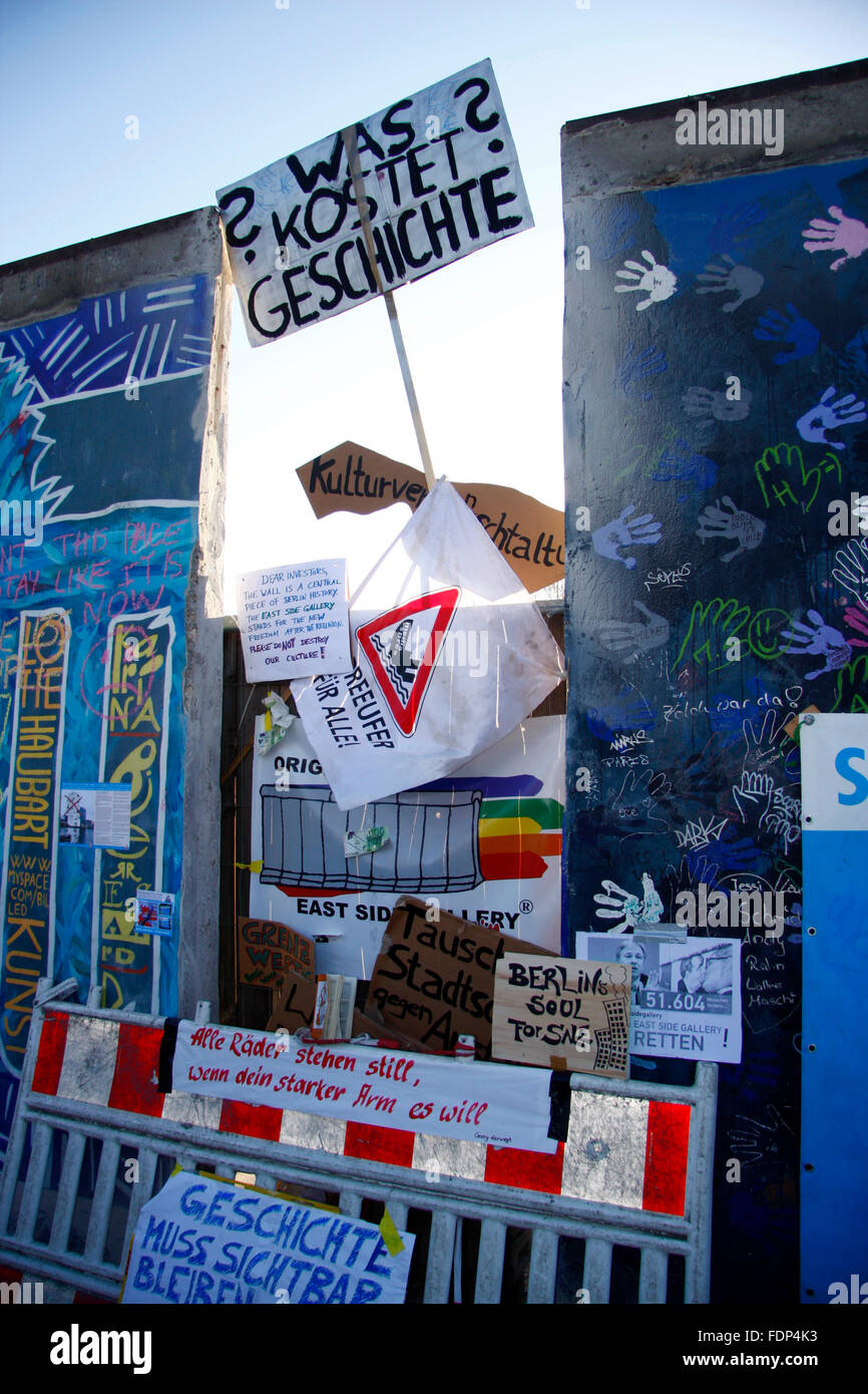 'Was kostet Geschichte?' - Protestplakate an einem Mauerstueck der Berliner Eastside Gallery, an dem ein Stueck fuer eine Zufahr Stock Photo
