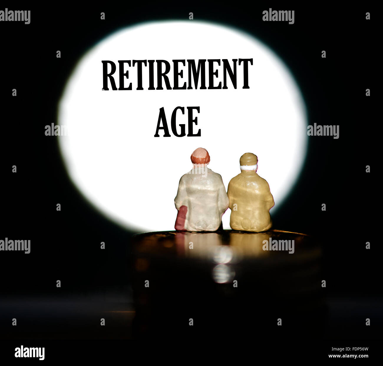Miniature figurine pensioners sitting on coins in front of a spotlight showing the words Retirement age concept Stock Photo