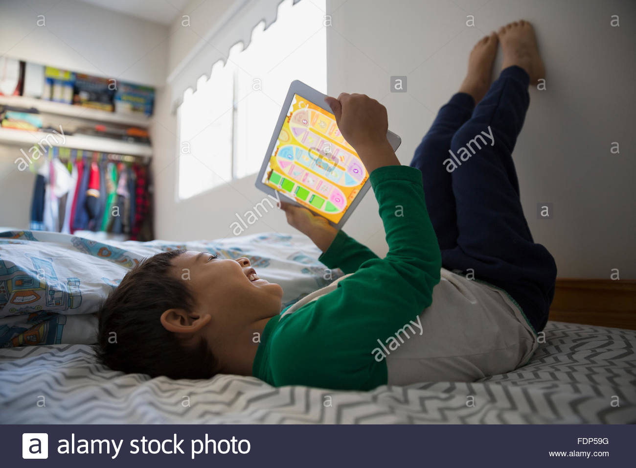 Boy feet up using digital tablet on bed Stock Photo