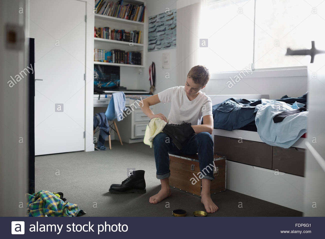 Boy shining cadet uniform shoes in bedroom Stock Photo