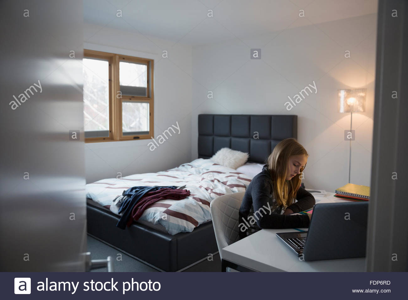 Girl doing homework at laptop in bedroom Stock Photo