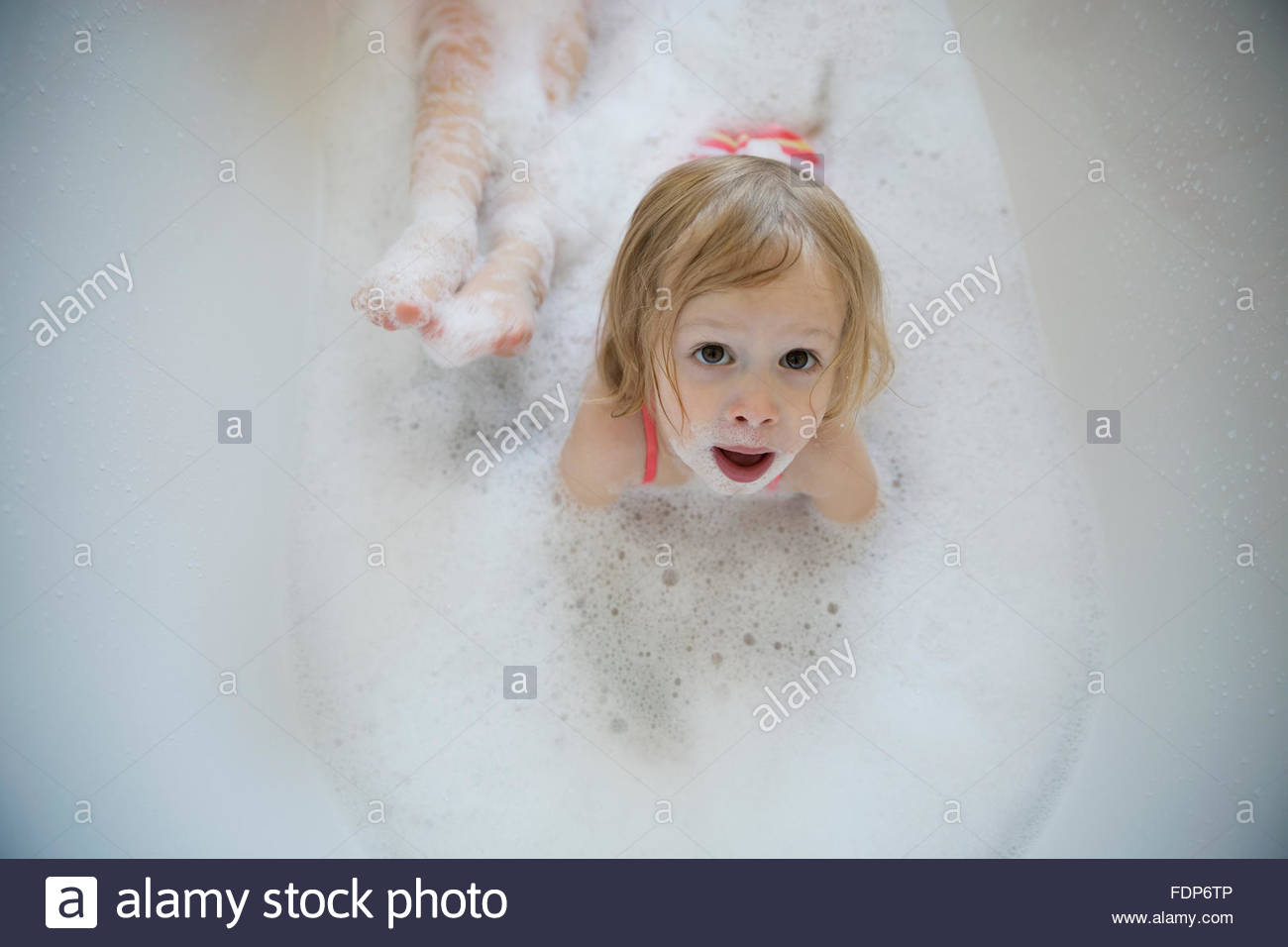 Overhead portrait wide-eyed girl laying bubble bath Stock Photo