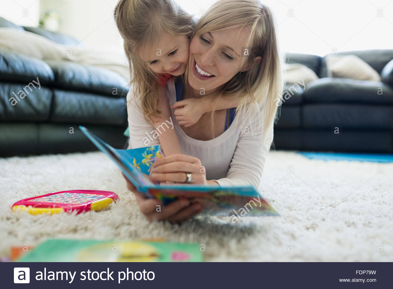 Daughter laying top mother reading book rug Stock Photo