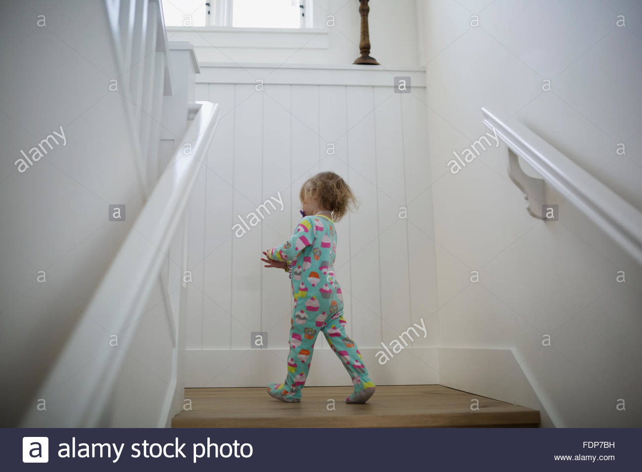 Girl in onesie pajamas on staircase landing Stock Photo
