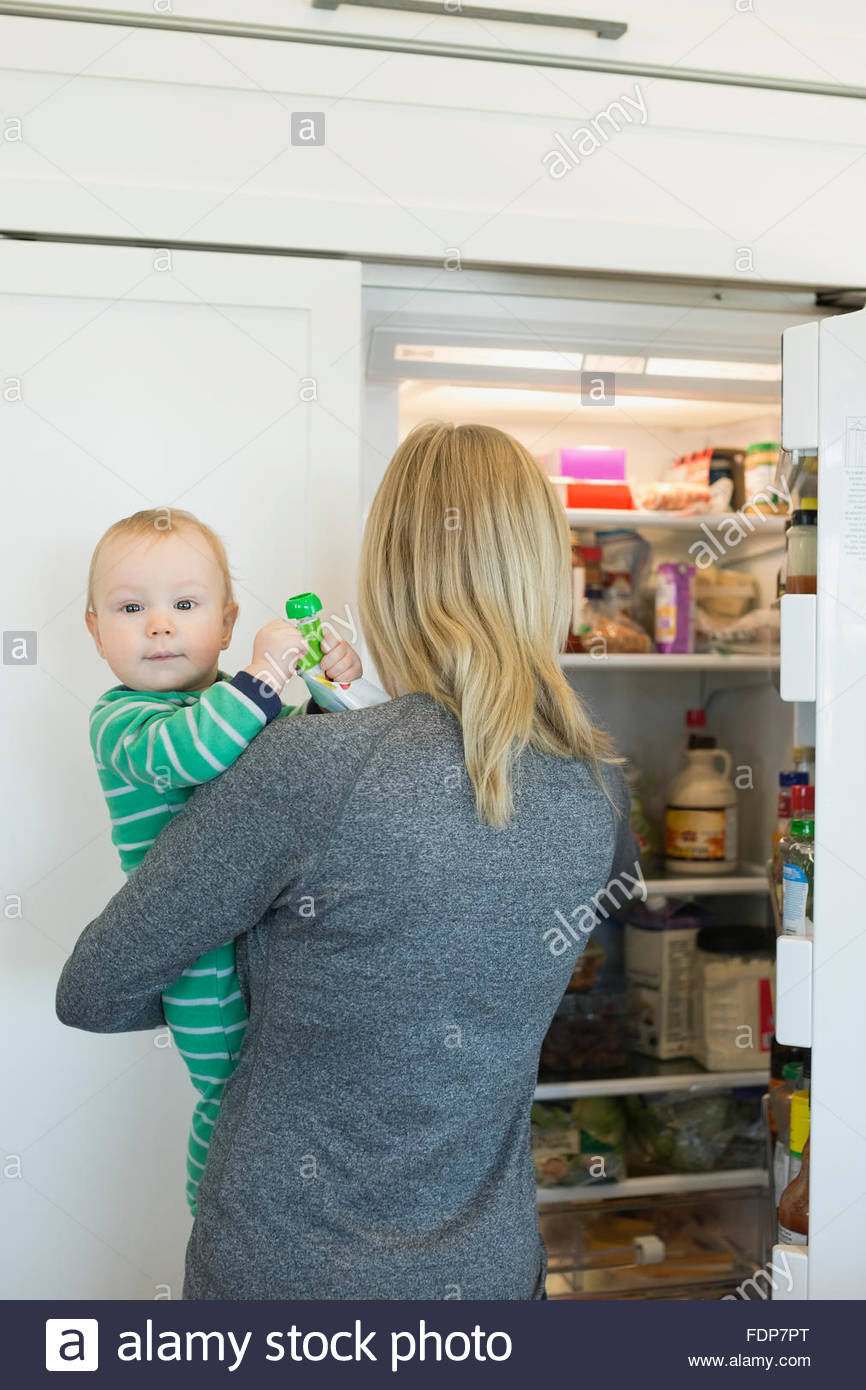 Mother holding baby son at open refrigerator Stock Photo