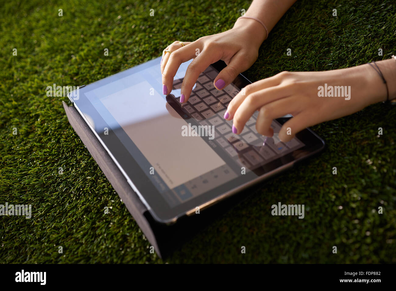 Closeup view of young woman writing on tablet pc on grass, typing an email on digital screen. Stock Photo