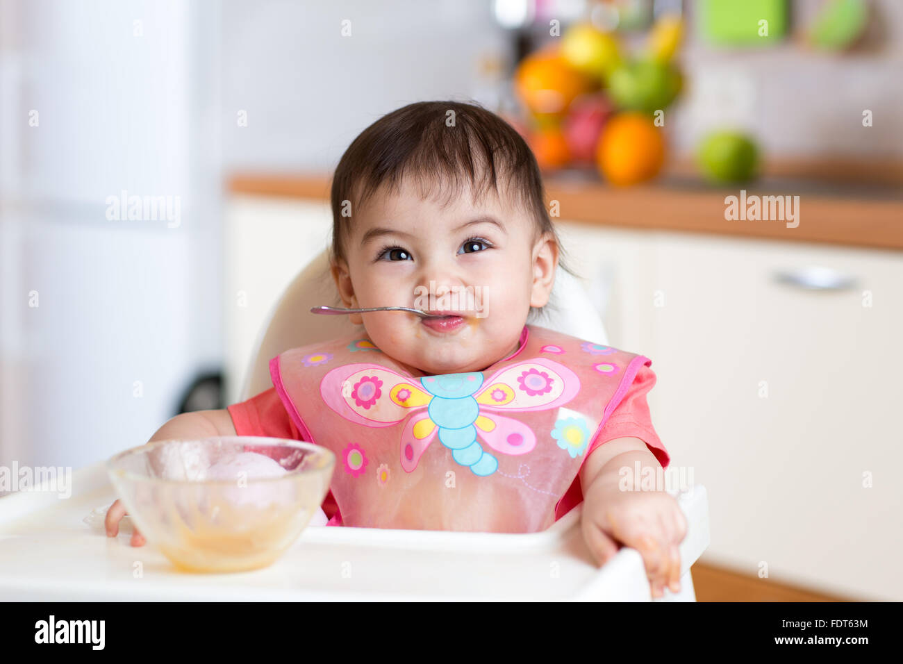 funny baby child eating itself with spoon in kitchen Stock Photo