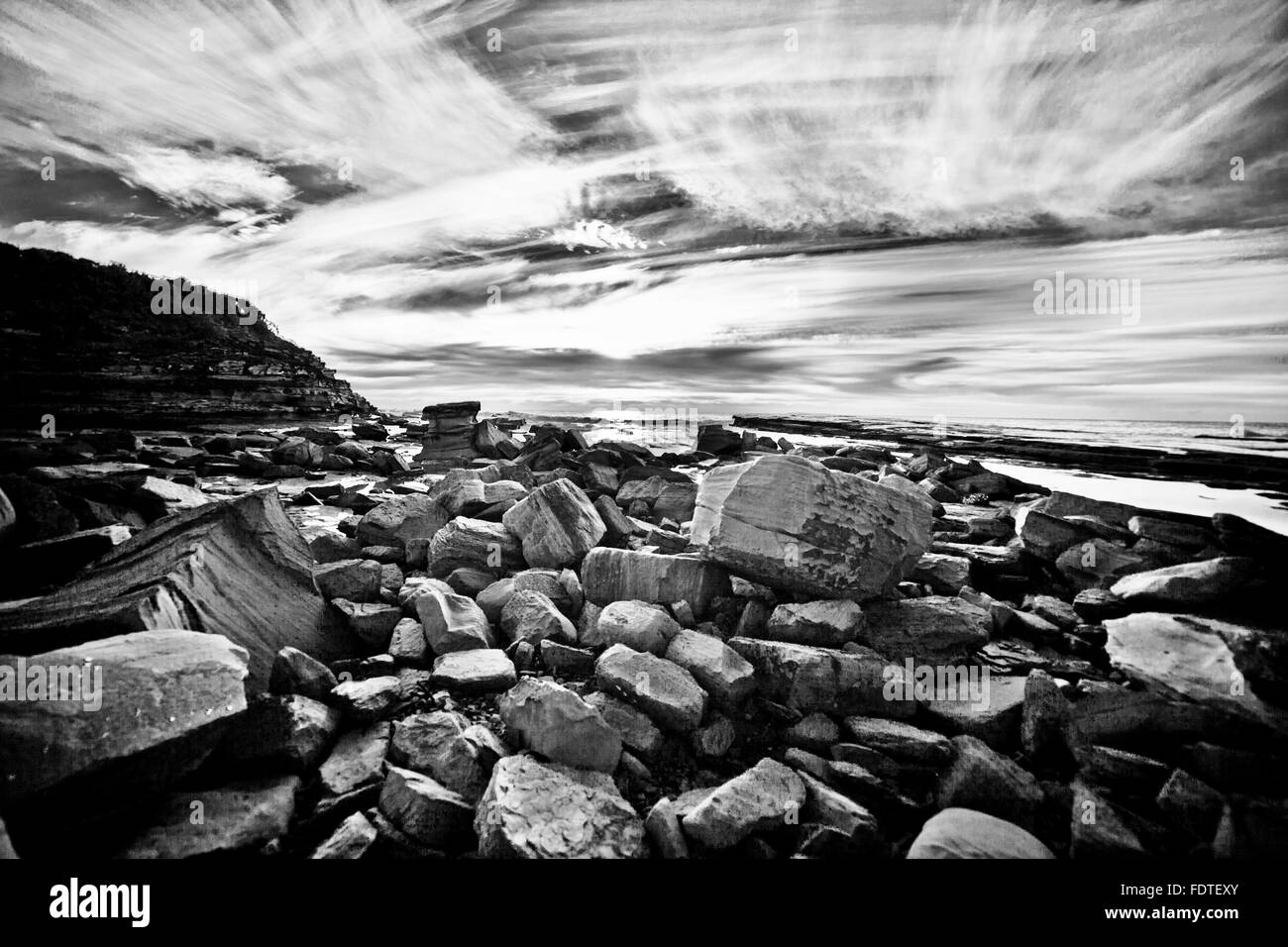 black / white picture of rocks on the sea shore with dramatic cloudy sky Stock Photo