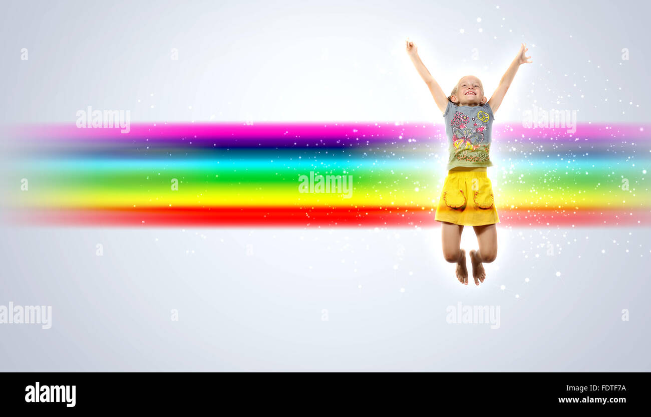 Photo of little girl jumping and raising hands against rainbow