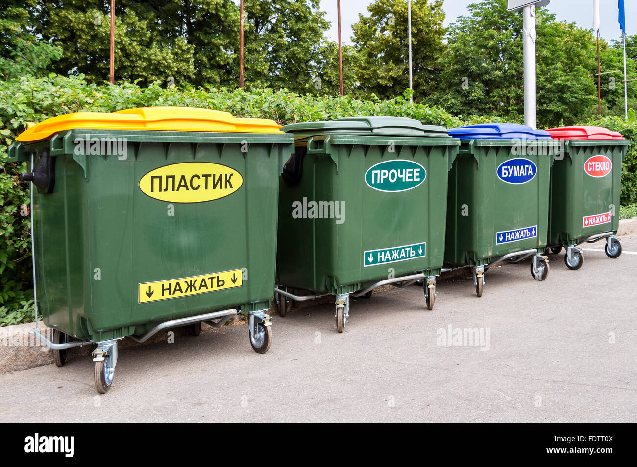 Green dumpsters on a city street. Text in russian: " Plastic", "Other", "Paper", "Glass", "Press on" Stock Photo