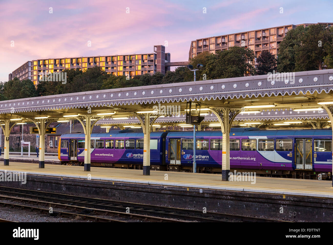 Northern train at Sheffield Railway Station as night approaches with Park Hill flats lit by evening light in the distance, Sheffield, England, UK Stock Photo
