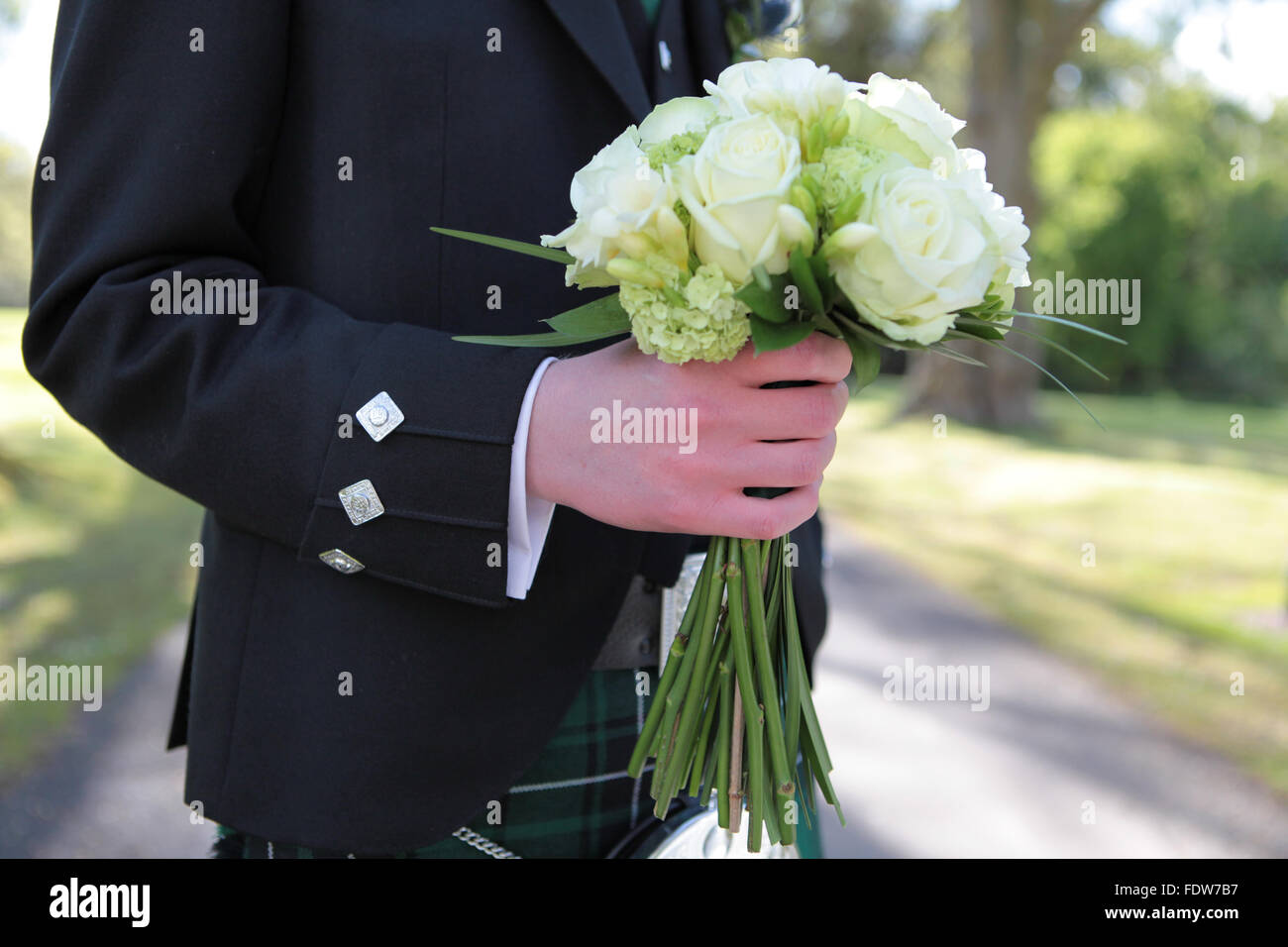 Groom in traditional Scottish wedding outfit holding the brides bouquet Stock Photo