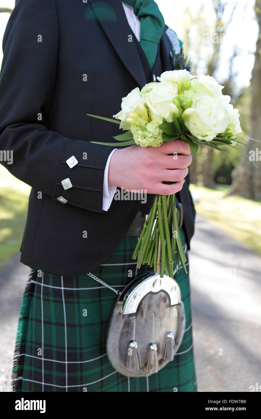 Groom in traditional Scottish wedding outfit holding the brides bouquet Stock Photo