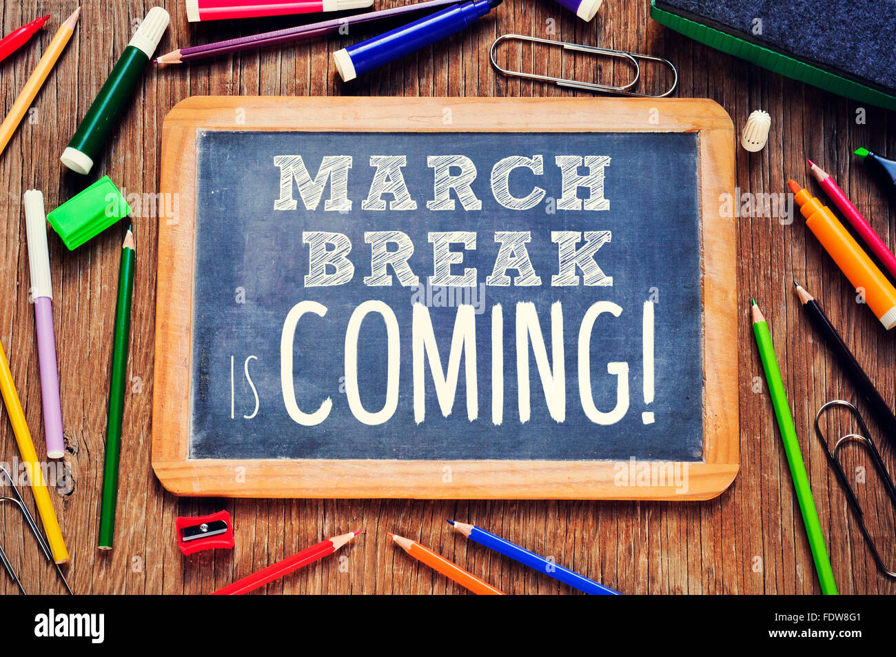 high-angle shot of a rustic wooden table with some pencils and markers and a chalkboard with the text march break is coming writ Stock Photo