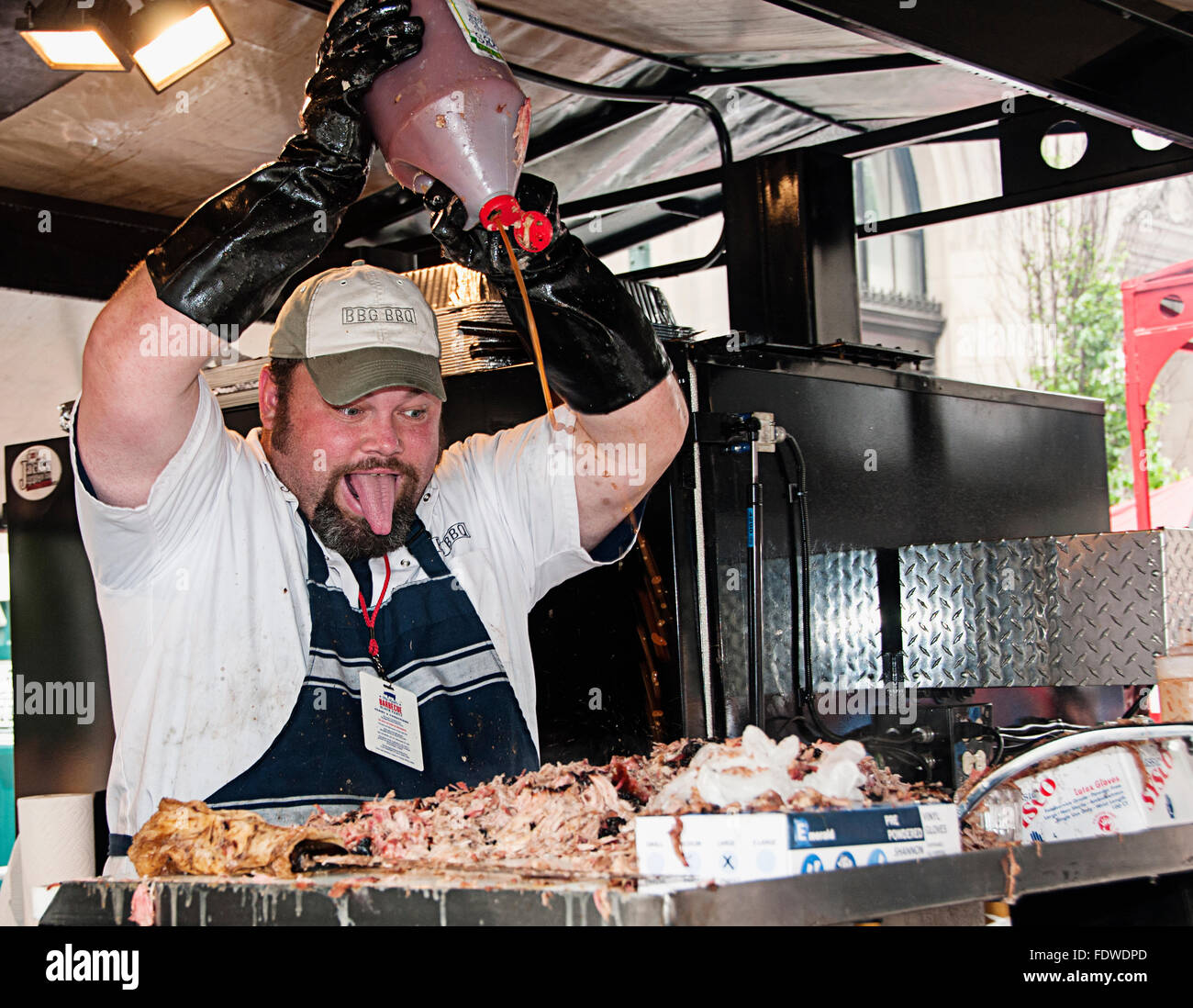 A pit cook at the BBG BBQ truck at the Big Apple BBQ spraying BBQ sauce on pulled pork. Stock Photo