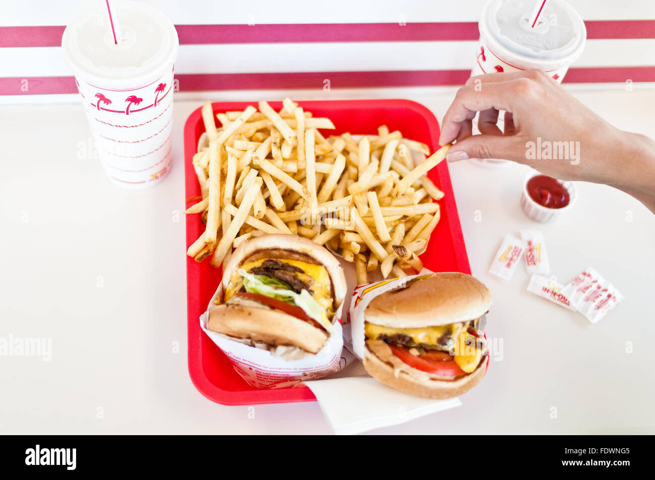 A hand takes a french fry from a tray of cheeseburgers and fries waiting to be eaten at In-N-Out Burger, Los Angeles, California Stock Photo